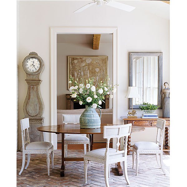 Gerrie Bremermann is known for her affinity for a white palette and her love of antiques, particularly French, such as this 19th-century wine table that mingles with Swedish chairs and clock. | Photo by Tria Giovan