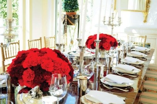 Dining table set for a formal dinner with red flower arrangements