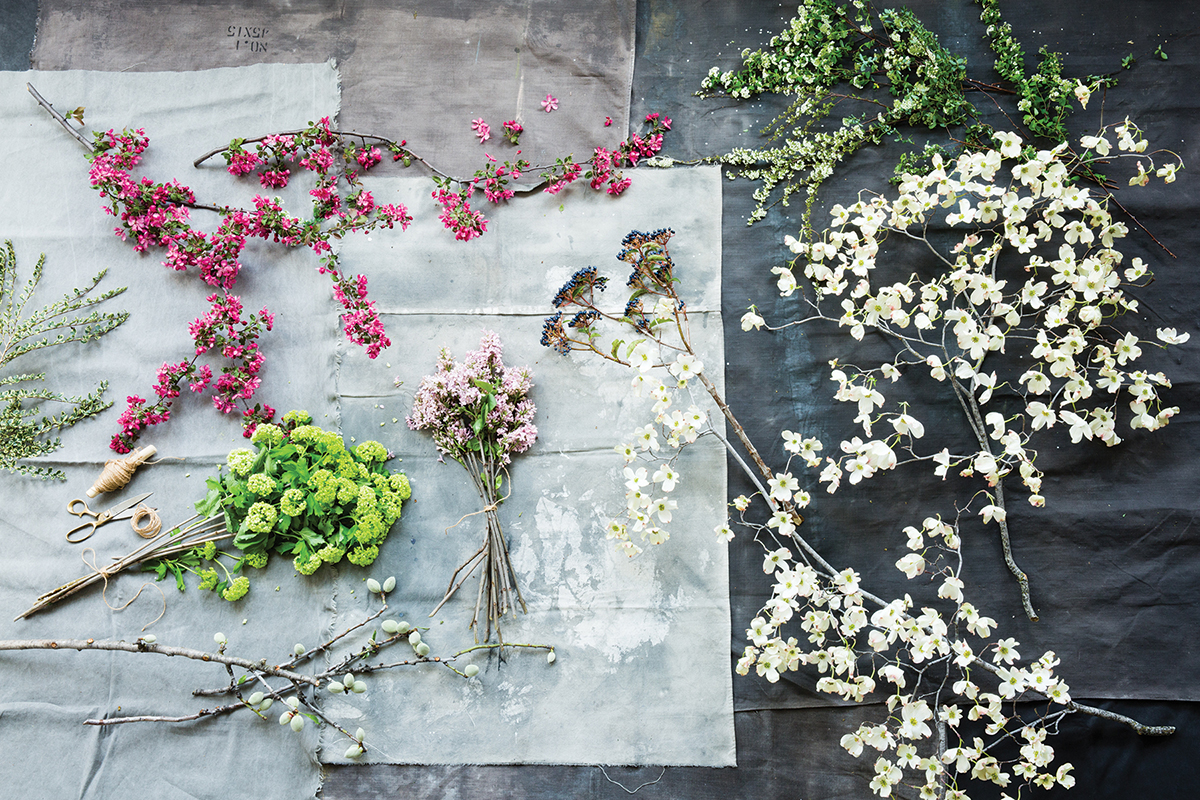 assorted flowering branches with white, green, hot pink, and light pink flowers, spread out on a wooden work surface