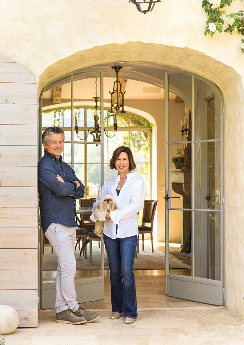 Brooke and Steve Giannetti stand at the entrance of their home. Steel-and-glass doors allow the eye to travel through the entryway to the gardens beyond.