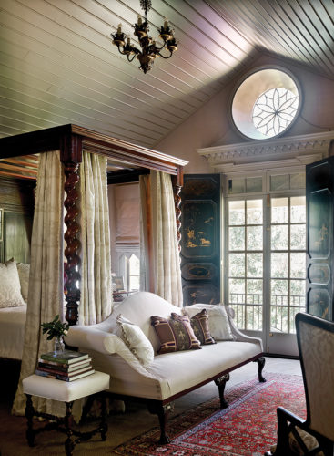 Lanham placed a Chippendale sofa at the foot of a reproduction 19th-century English barley-twist bed. The wrought-iron oculus was originally an attic vent.