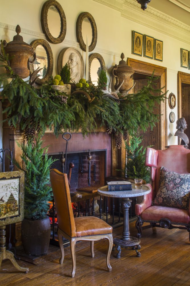 Great hall fireplace decorated with boughs of greenery and flanked by a pair of potted conifers.