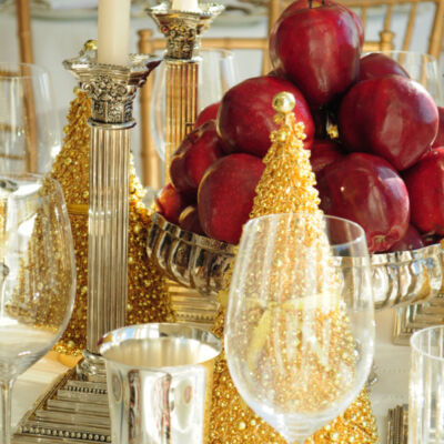 Table setting with silver cups, wine glass, gold Christmas tree, candlesticks, and bowl of fruit