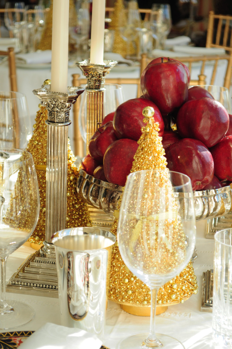 Table setting with silver cups, wine glass, gold Christmas tree, candlesticks, and bowl of fruit