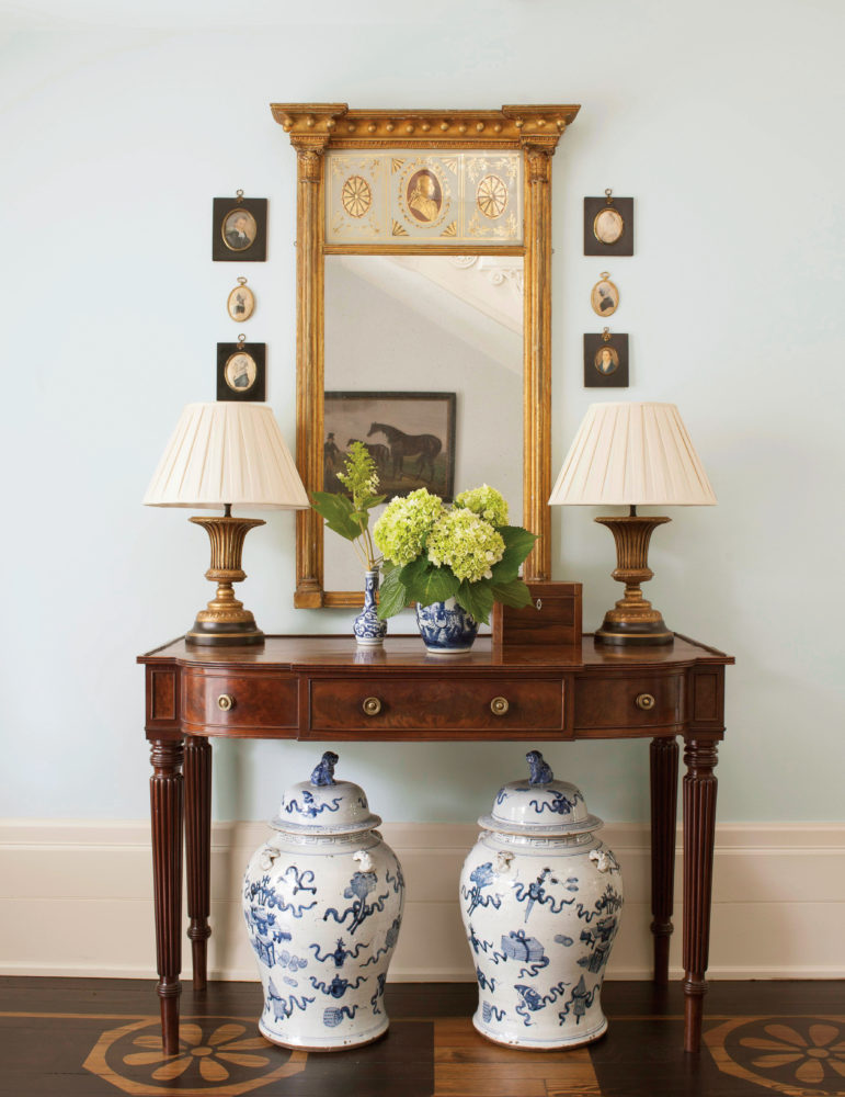 Antique console with mirror flanked by miniature portraits. Hardwood floor is painted with a stenciled pattern.