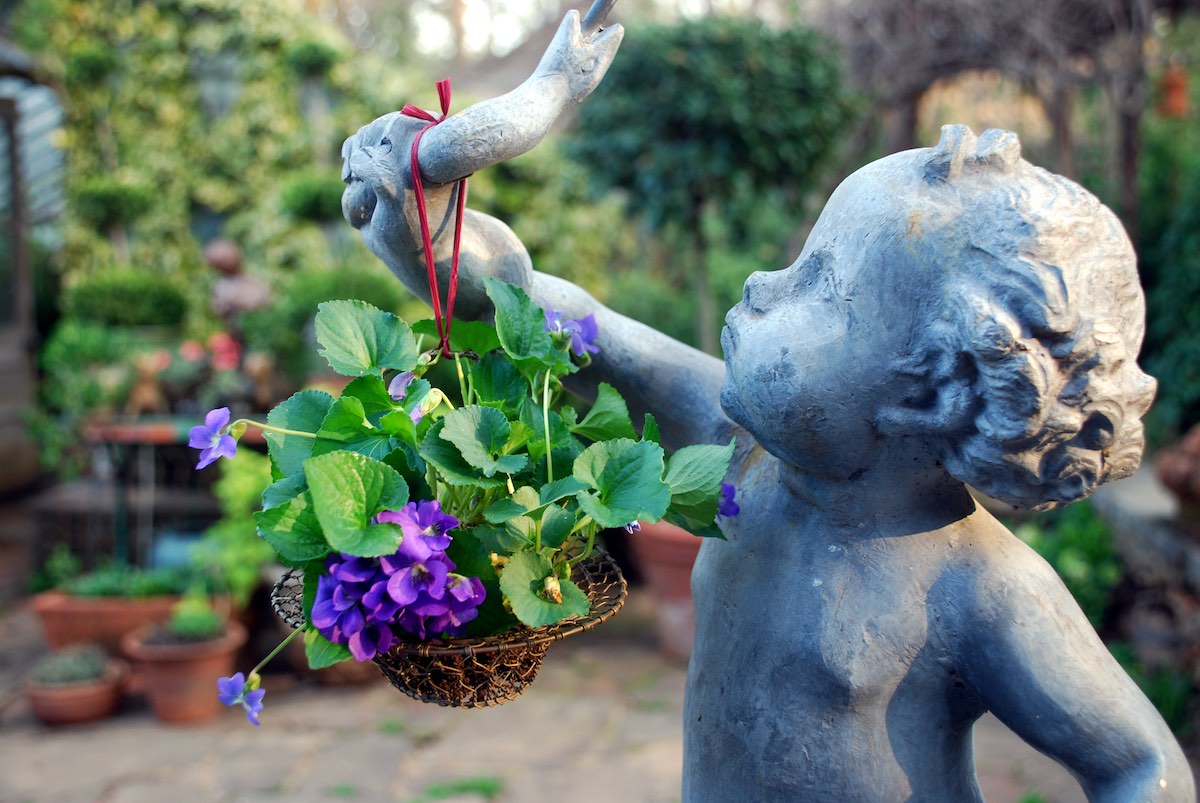 A cherub in Ryan Gainey's garden holds a container of violets.