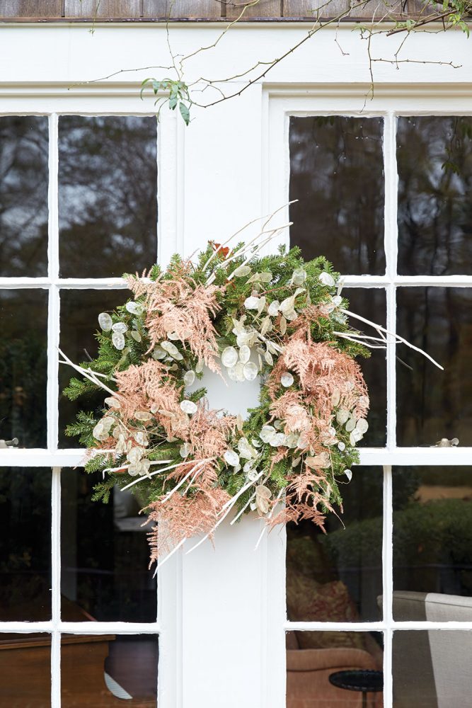 A window wreath speaks to the colors inside with lunaria (money plant), an abundance of bronzed asparagus feathers, and flocked mitsumata.
