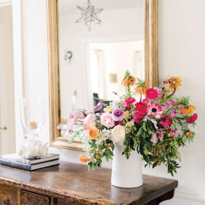 A large gilt framed mirror hangs above an antique wood console in a foyer by alecia stevens, interior designer