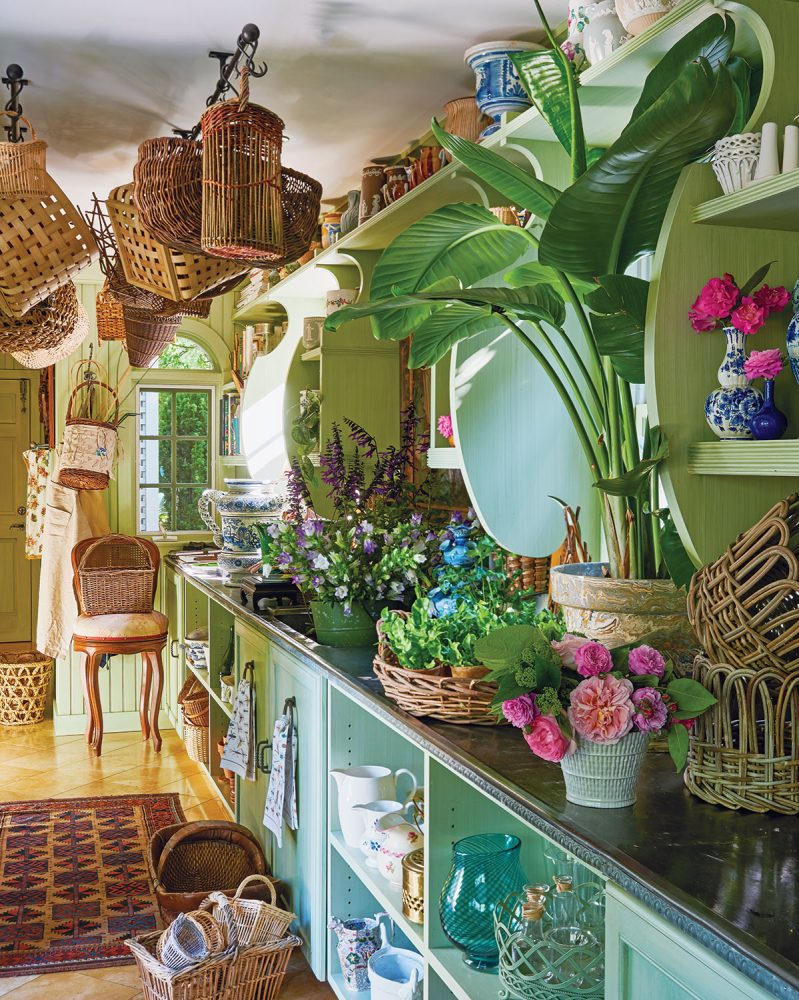 Charlotte Moss's flower room with light green cabinetry, zinc countertops loaded with flowers, and shelves of vases.