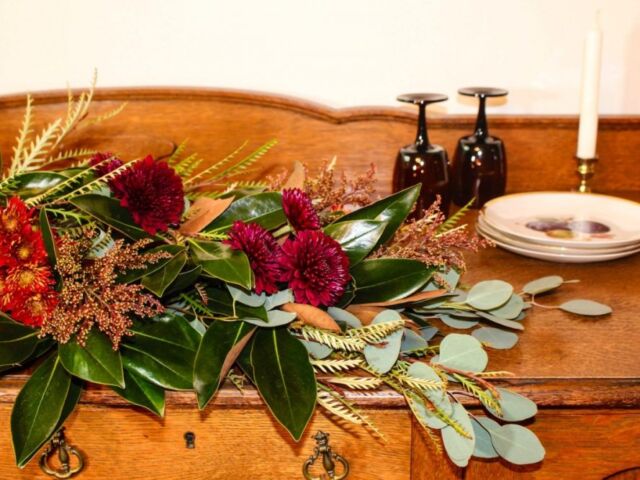 Thanksgiving table garland made with assorted chrysanthemums, dyed solidago, grevillea foliage, magnolia leaves, and silver dollar eucalyptus