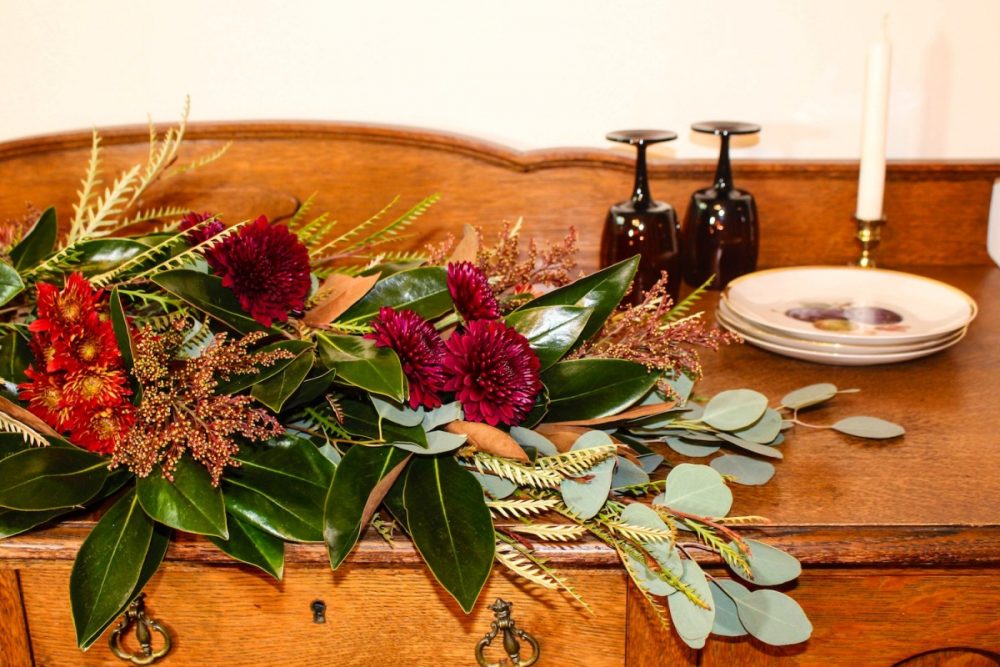 Thanksgiving table garland made with assorted chrysanthemums, dyed solidago, grevillea foliage, magnolia leaves, and silver dollar eucalyptus