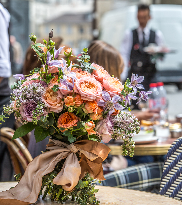 A French-style bouquet of peach and purple blooms sits on an outdoor table at a cafe in Paris