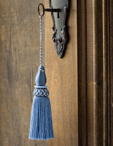 blue decorative tassel hanging from a key in a natural-finish wood door