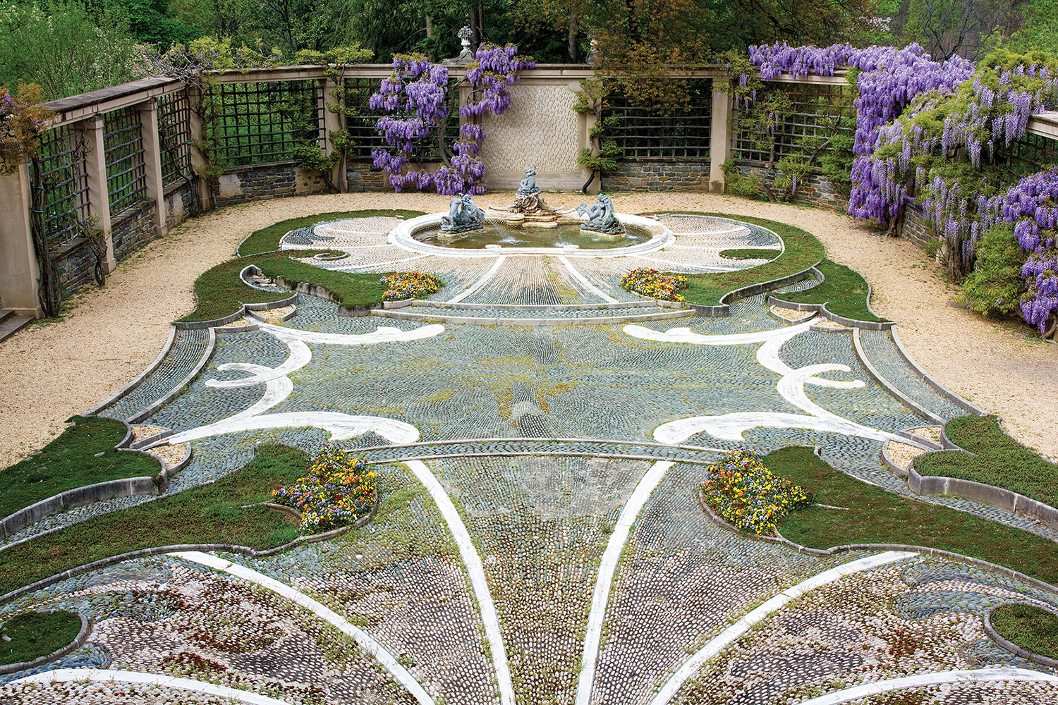 Intricate pebble hardscape featuring curvy inlays of grass and plantings, anchored by a fountain at one end.
