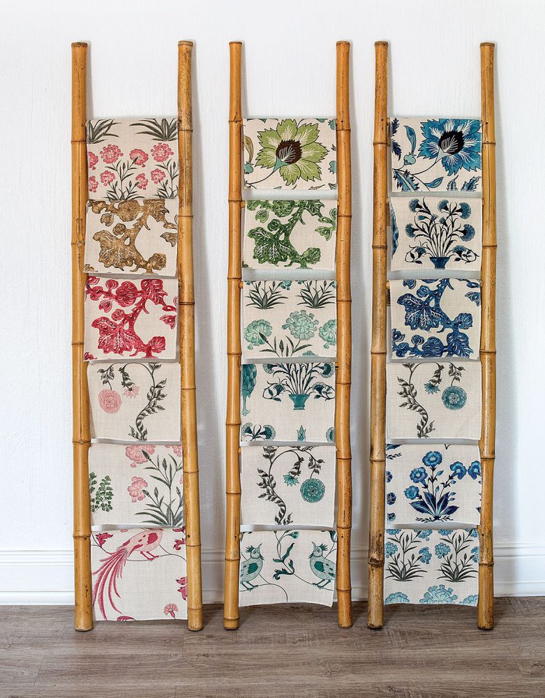 Assorted pink, green and blue botanical print textiles, designed by Debby Tenquist of Botanica Trading, hang on bamboo display racks