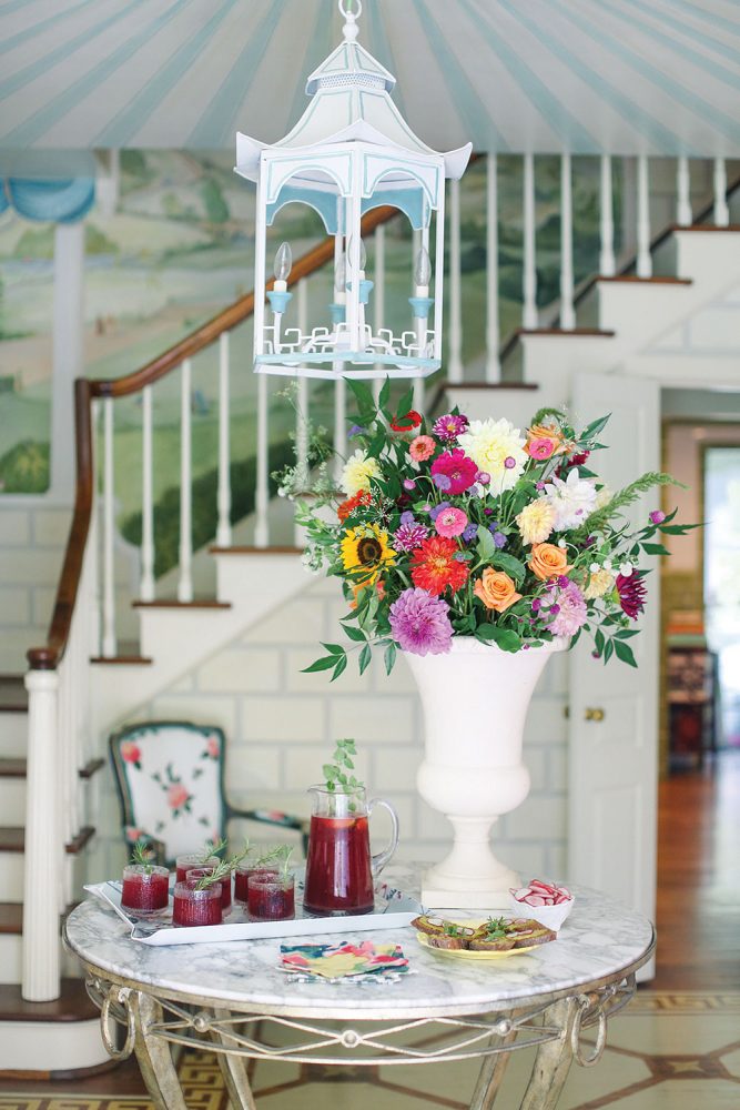 A round marble-top table with an elegant metal base holds a vase of flowers and tray of cocktails to greet party guests in the cottage's foyer