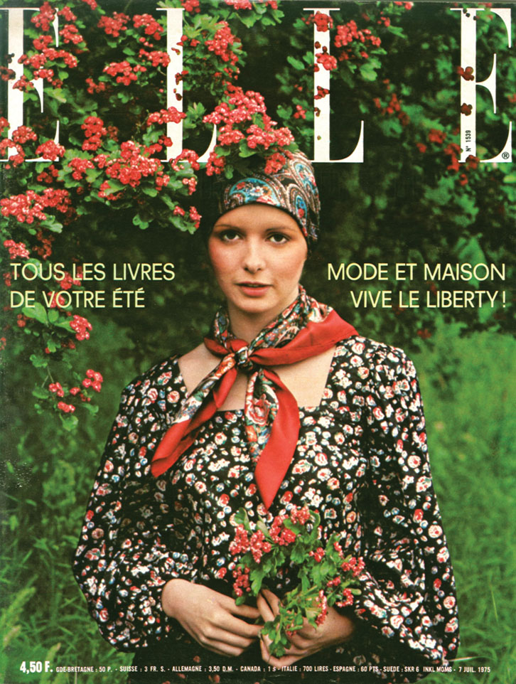 1975 Elle France magazine cover featuring a model wearing a Liberty botanical-print head scarf, neck scarf and dress, standing by a flowering shrub and holding a small bouquet of red flowers.