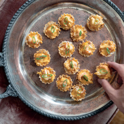 A hand grabs a Crawfish Cardinale Tart, a recipe by Julia Reed, from the tray