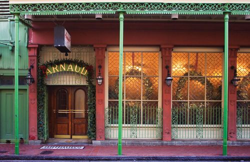 Red exterior of Arnaud's Restaurant in the French Quarter. It has a classic New Orleans iron balcony that's painted a bright green, as well as leaded windows