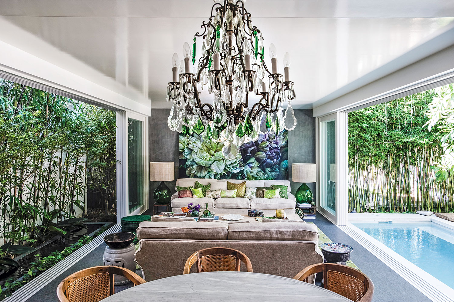 One of the home's indoor-outdoor living spaces, the open-air living room includes the dining table and chandelier, two sofas facing each other, and, on the back wall, a large floral painting by Marcella Kaspar.