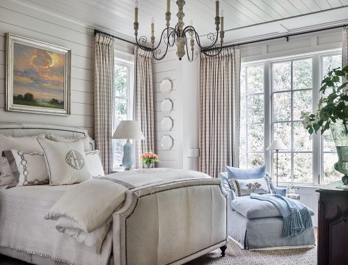 The master bedroom’s white-on-white palette gains depth from layers of contrasting textures, including rough shiplap walls, smooth porcelain plates, and the coarse hair-on-hide bed. A blue chaise with matching throw and a glazed lamp add a pop of light blue, while a landscape painting featuring a morning sky also breaks up the neutral palette.