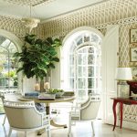 The room features a tray ceiling, arched french doors, a table and three chairs, a wood floor painted in a light gray and white diamond pattern, and a small indoor tree with large green leaves in a blue-and-white porcelain pot.