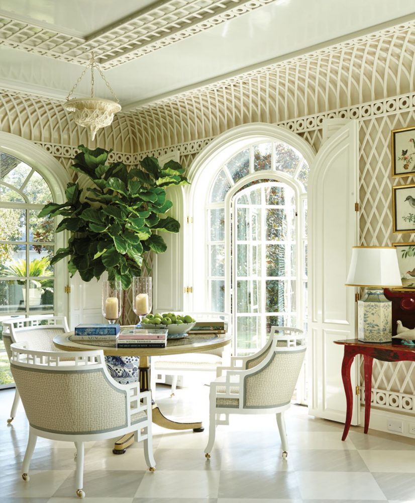 The room features a tray ceiling, arched french doors, a table and three chairs, a wood floor painted in a light gray and white diamond pattern, and a small indoor tree with large green leaves in a blue-and-white porcelain pot.