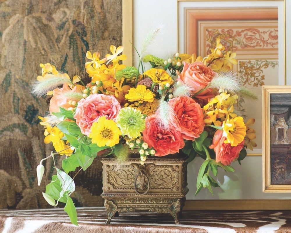 Arrangement of green, yellow and orange/coral blooms in an antique-looking brass box