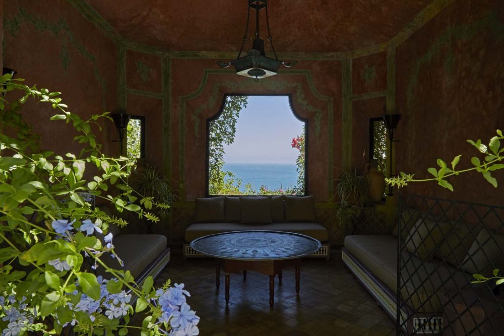 An ocean view framed by an ornate, but simply furnished sitting room with banquets on three walls around a low circular table