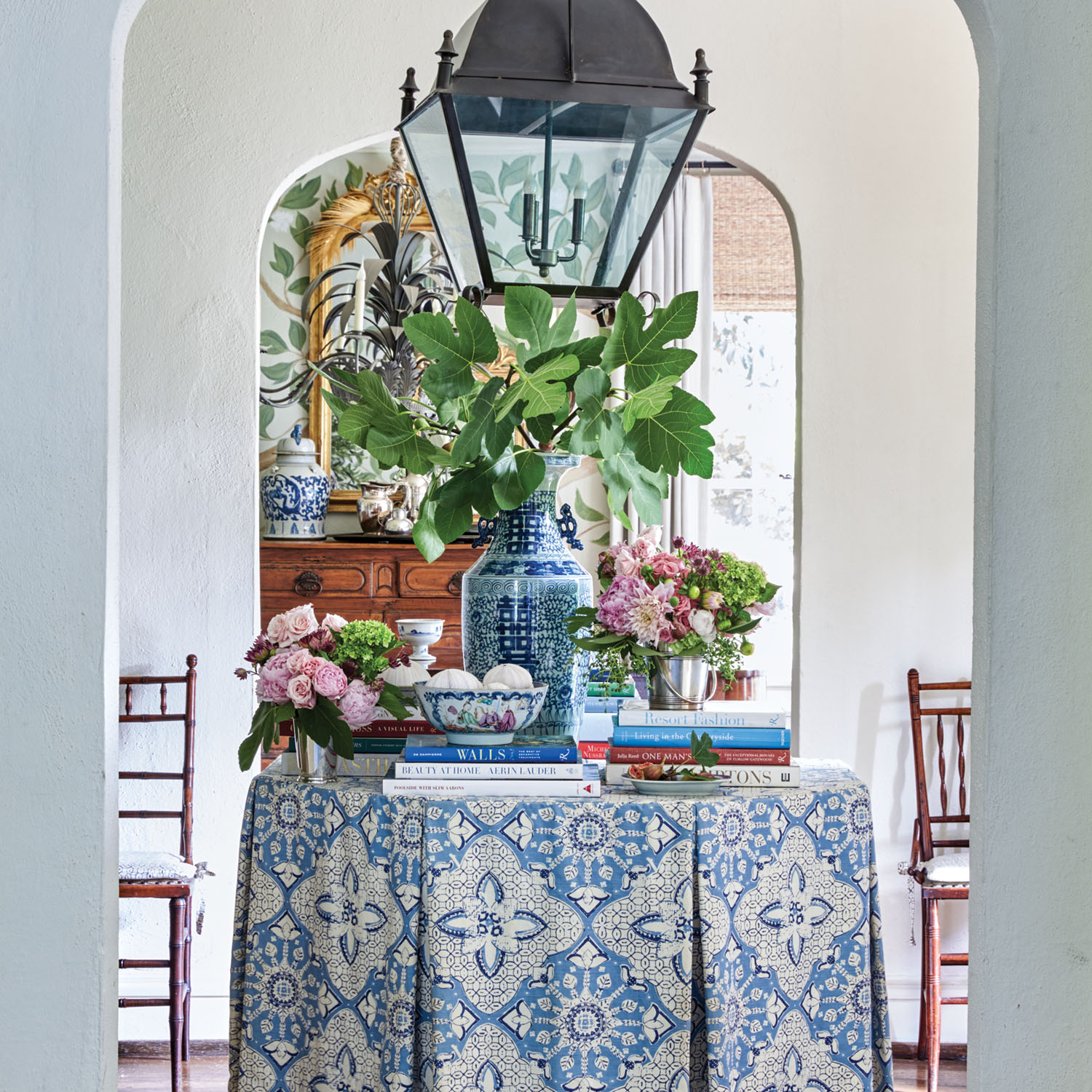 A round table in an entry is topped with a tailored blue-and-white table skirt, blue-and-white pottery, books, and floral arrangements.