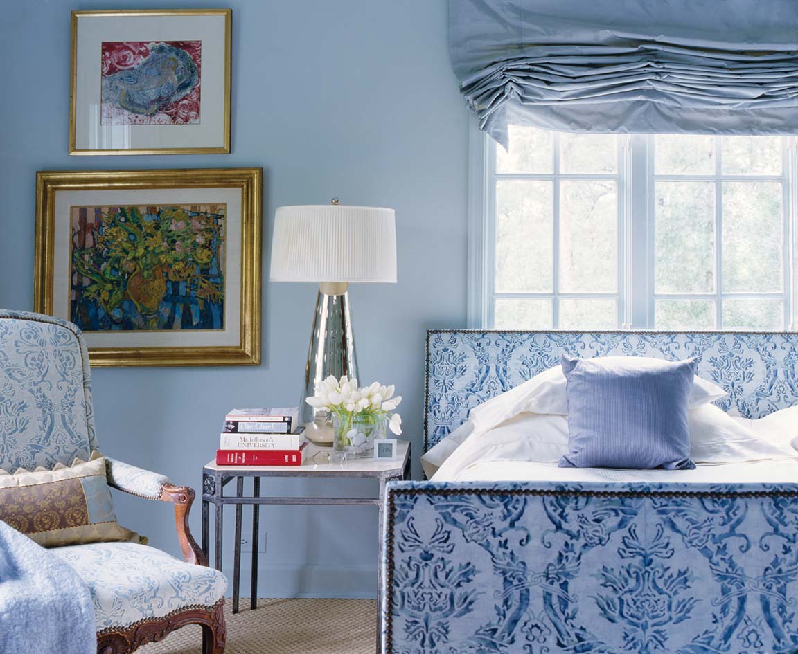 Bedroom in blue and white with vase of white tulips on bedside table with tall silver lamp