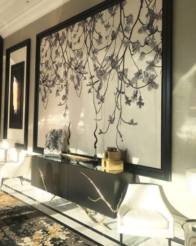 Awash in dappled sunshine, the hotel hallway furnished with a modern sideboard, two sleek white chairs, and asian botanical screen, and an oriental rug
