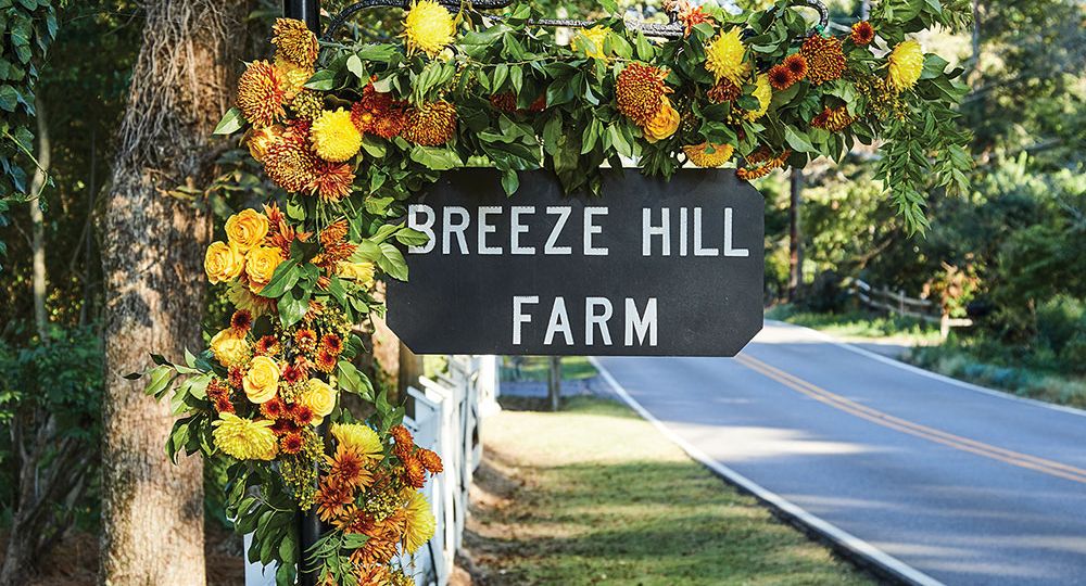 Sign for Breeze Hill Farm decorated with orange and yellow flowers