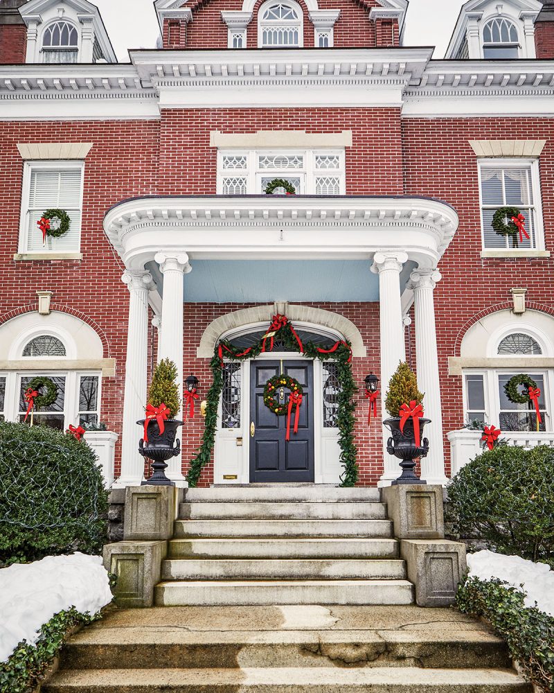 Historic brick home decked with garland and Christmas tree topiaries on either side of the front door