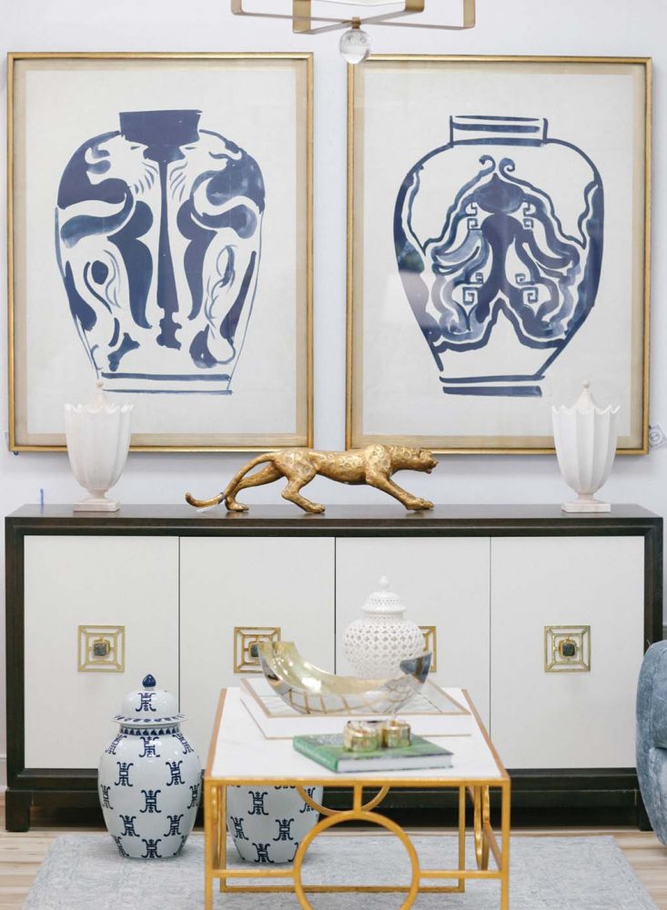 A shop scene from Beckon Home in Richmond, Virginia, including abstract art prints of large blue-and-white ginger jars, a modern console and a modern coffee with a gold metal vase, and other decorative accessories.