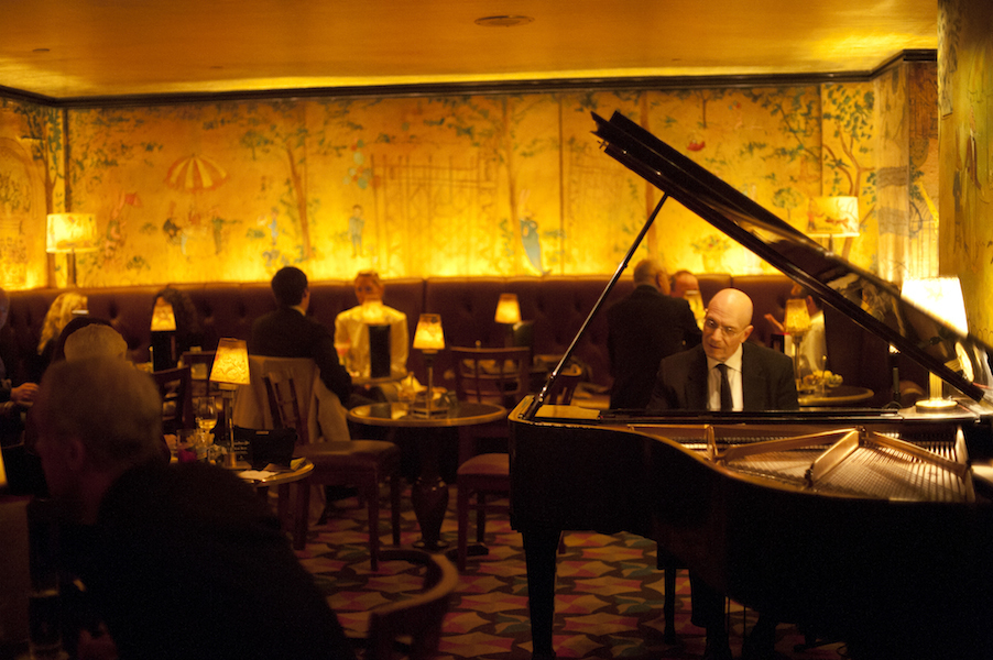 A piano player performs in a dimly lit, scenic wallpaper-wrapped dining area of Bemelmans Bar in New York City