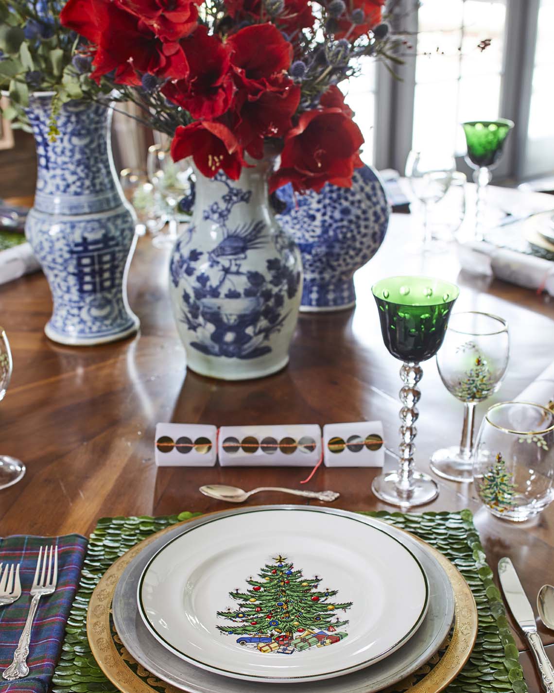 A table set with Christmas tree-themed china and green glass goblets