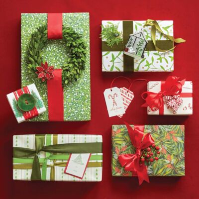 Red and green holiday gift wrap ideas. Adornments attached to ribbons include a large green button, a small green wreath, faux peppermint candies, a blown glass tree ornament, and a greenery sprig.