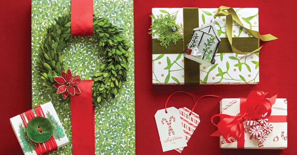 Red and green holiday gift wrap ideas. Adornments attached to ribbons include a large green button, a small green wreath, faux peppermint candies, a blown glass tree ornament, and a greenery sprig.