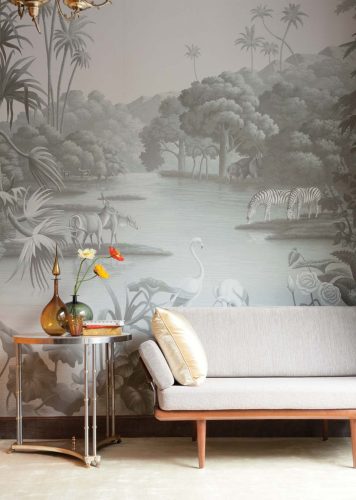 De Gournay wallpaper in a gray color palette featuring birds, zebras, and other African animals gathered around a tree-lined watering hole