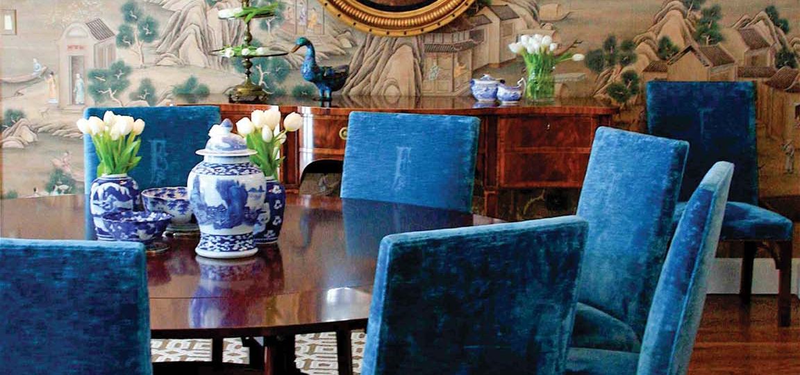 Dining room featuring deep blue velvet chairs around a circular table, a geometric print rug, a convex gold-framed circular mirror above the side board, and Gracie’s ‘Ming Village' wall covering