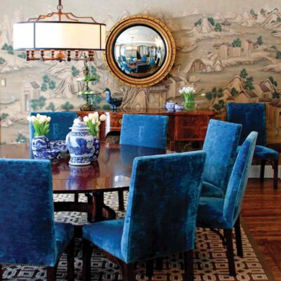 Dining room featuring deep blue velvet chairs around a circular table, a geometric print rug, a convex gold-framed circular mirror above the side board, and Gracie’s ‘Ming Village' wall covering
