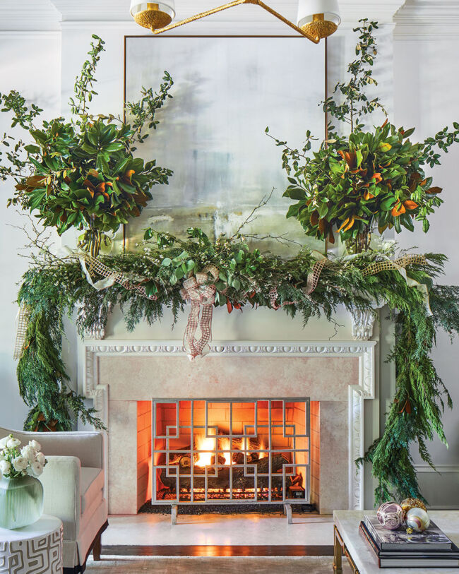 lush garland and two large vases of greenery, with ribbon accents, decorate a holiday mantel