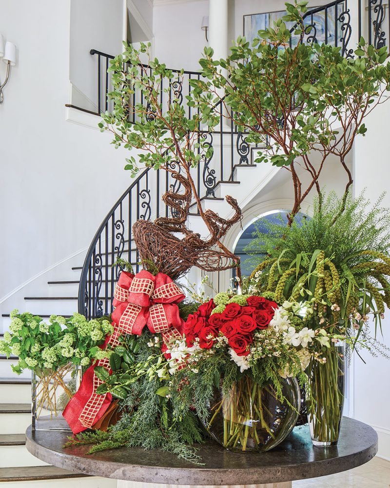 A grand Christmas floral display files a circular table. In the background, a staircase with black iron railing curves around the wall of the rotunda. 