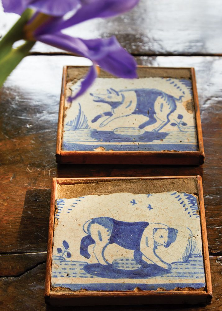 The age-worn pair of blue-and-white tiles, which depict a bear and a wolf, are displayed in thin individual frames set on a glossy wood plank surface in the book ‘Near & Far’ by Lisa Fine