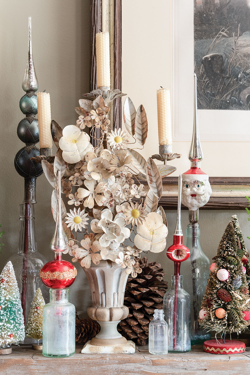 Holiday vignette with vintage blown-glass tree toppers in old bottles, retro-style small decorative Christmas trees, and a Tole candleholder fashioned to look like a vase of cream-colored flowers in the home of event planners Rick Davis and Christopher Vazquez