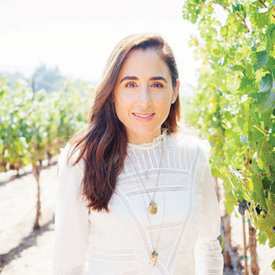 April Gargiulo, founder of Vintner's Daughter skin care, stands in a vineyard wearing a white 3/4-sleeve top and jeans