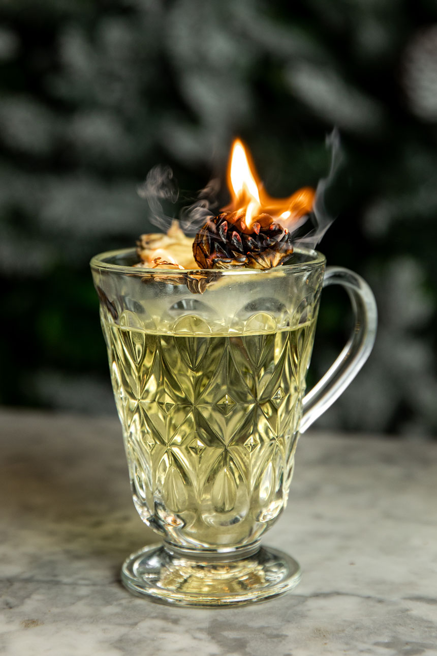 Dalloway Terrace's hot toddy is served in a crystal cup with a pedestal and handle. The herb garnish is set aflame for a wintry presentation