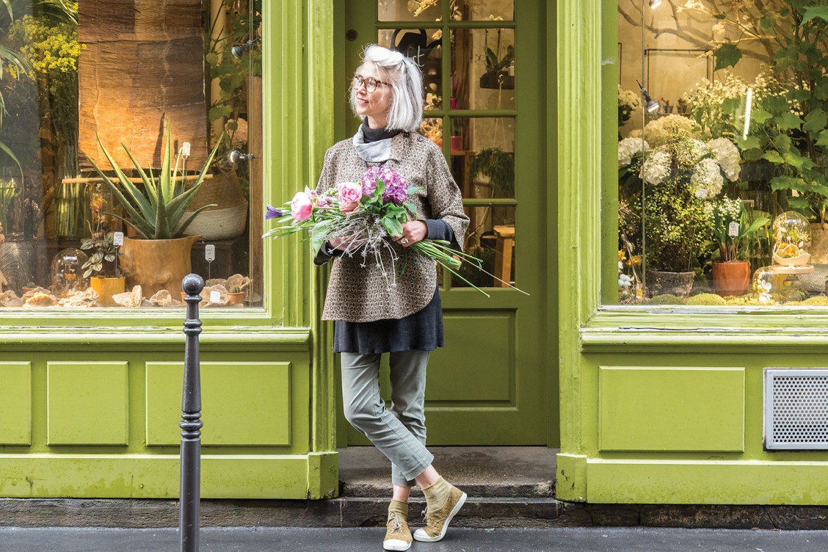 Parisian florist Clarisse Beraud stands casually in the doorway of her classic French storefront, with trim and a french door painted bright lime green.