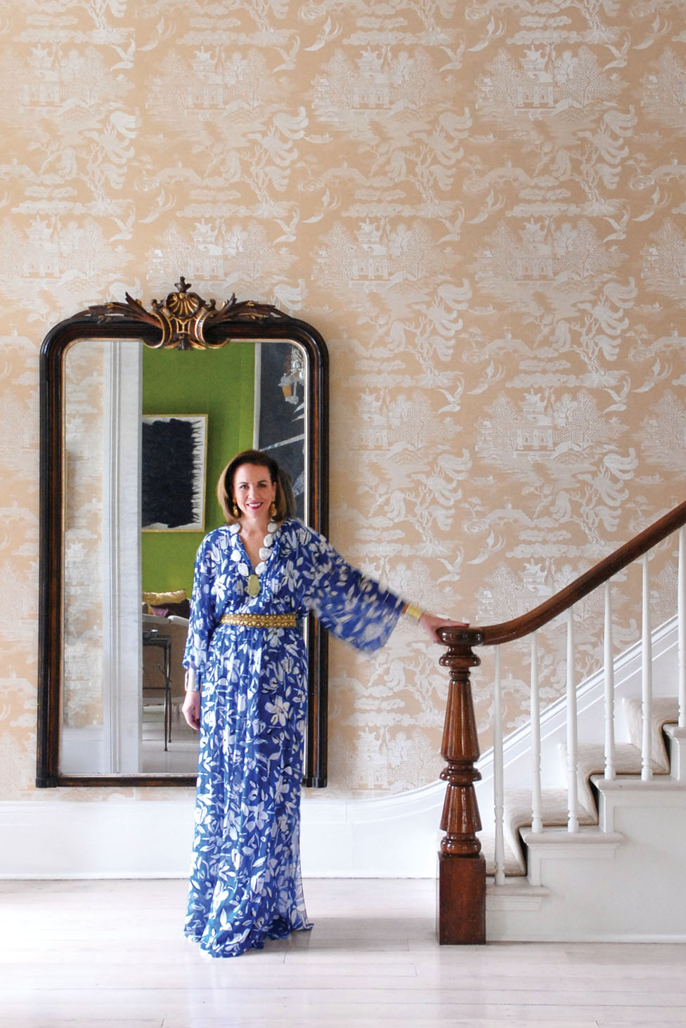 founder of Leontine Linens in a long blue floral print dress stands at the bottom of an elegant staircase
